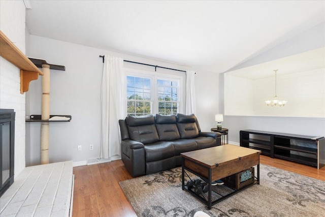 living area with an inviting chandelier, vaulted ceiling, wood finished floors, and visible vents