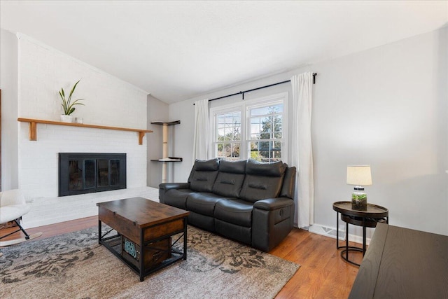 living room featuring a brick fireplace, wood finished floors, and vaulted ceiling