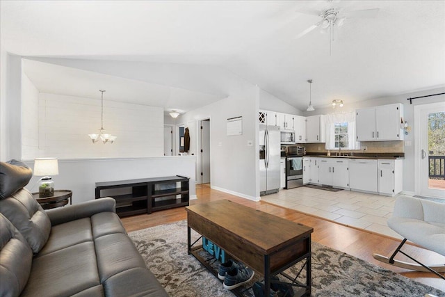 living area featuring light wood-type flooring, lofted ceiling, baseboards, and ceiling fan with notable chandelier