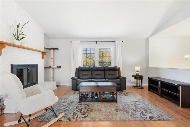 living area with a brick fireplace, lofted ceiling, baseboards, and wood finished floors