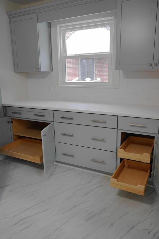 kitchen featuring decorative backsplash, marble finish floor, and gray cabinetry