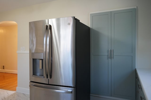 kitchen with baseboards, light stone countertops, wood finished floors, arched walkways, and stainless steel fridge