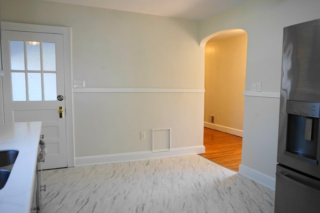 kitchen featuring wood finished floors, arched walkways, stainless steel fridge, and baseboards