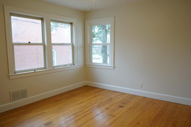 empty room with baseboards, visible vents, and light wood finished floors