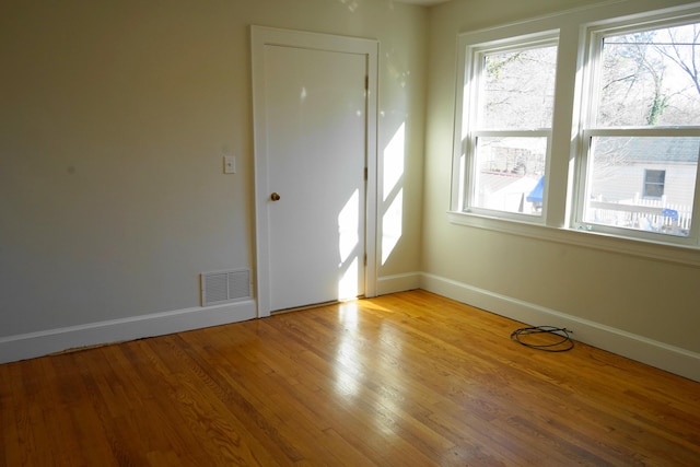 empty room featuring light wood-style floors, a healthy amount of sunlight, and visible vents