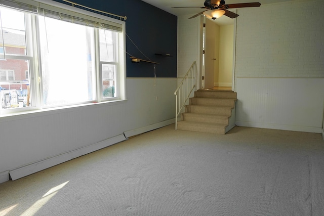 spare room with a wainscoted wall, carpet flooring, stairs, and ceiling fan