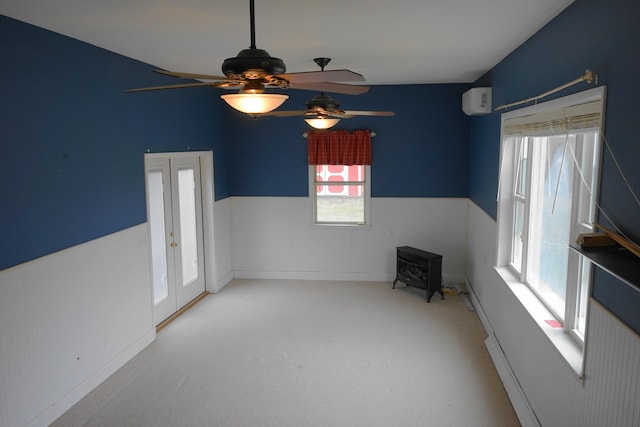 carpeted empty room featuring a wood stove, a ceiling fan, and wainscoting