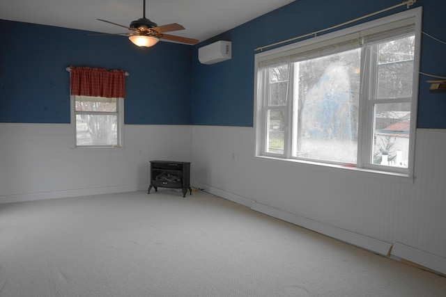 carpeted empty room featuring a ceiling fan, an AC wall unit, a wood stove, and a healthy amount of sunlight