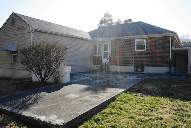 back of house with a patio area, brick siding, and a chimney