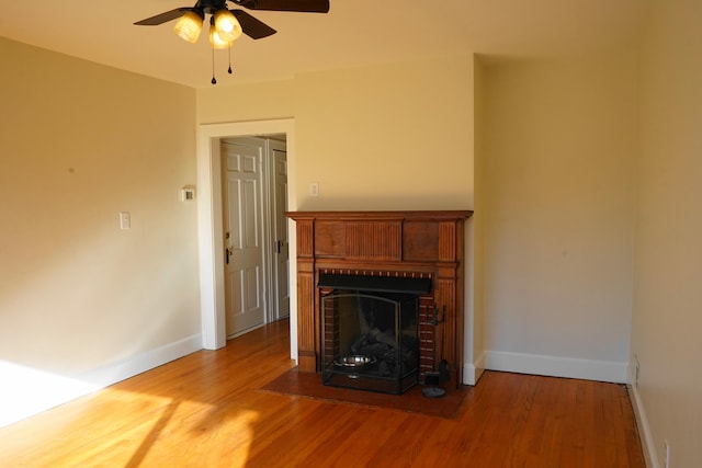 unfurnished living room with a brick fireplace, wood finished floors, baseboards, and ceiling fan