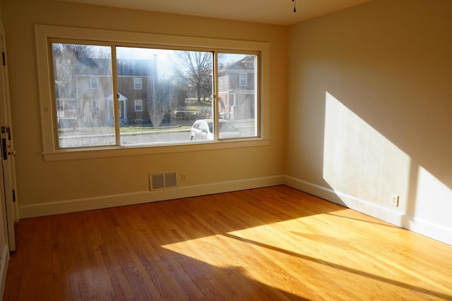 spare room with a wealth of natural light, visible vents, baseboards, and wood finished floors