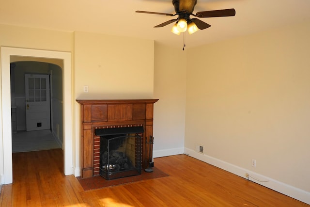 unfurnished living room featuring visible vents, a brick fireplace, baseboards, ceiling fan, and wood finished floors