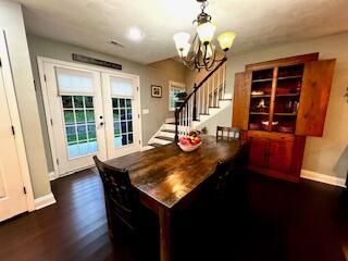 dining area featuring a notable chandelier, dark wood finished floors, french doors, stairway, and baseboards