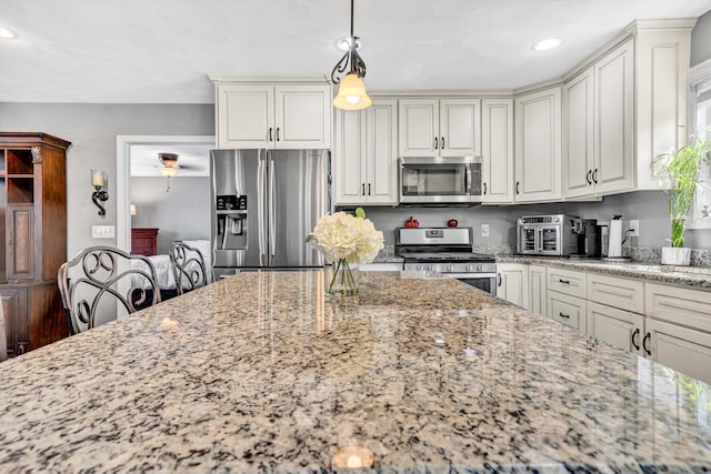 kitchen featuring pendant lighting, light stone counters, stainless steel appliances, and white cabinetry