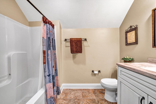 bathroom featuring lofted ceiling, stone finish floor, toilet, vanity, and baseboards
