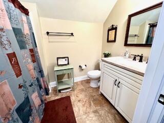 bathroom with baseboards, lofted ceiling, toilet, and vanity