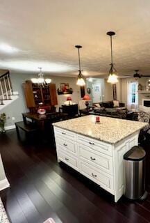 kitchen featuring a center island, dark wood-type flooring, light stone countertops, decorative light fixtures, and white cabinets