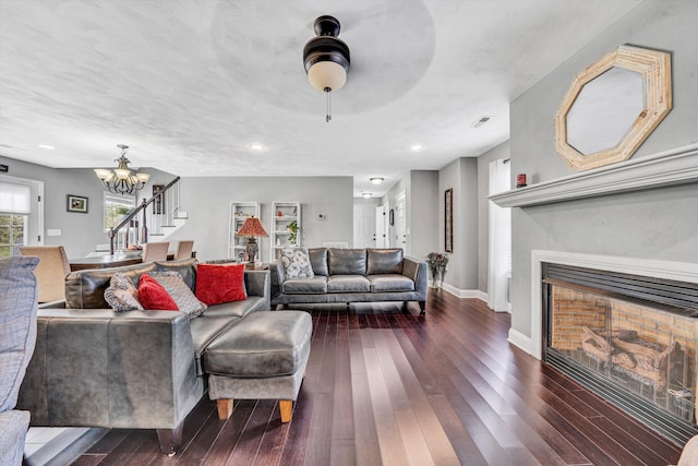 living room featuring dark wood-style floors, baseboards, an inviting chandelier, stairs, and a fireplace