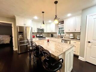 kitchen with a kitchen island, a kitchen bar, appliances with stainless steel finishes, hanging light fixtures, and white cabinetry