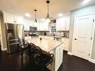 kitchen featuring a center island, pendant lighting, a kitchen bar, appliances with stainless steel finishes, and white cabinetry