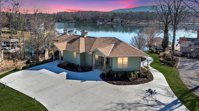 view of front facade featuring a shingled roof, a water view, driveway, and a chimney