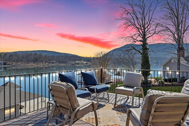 patio terrace at dusk featuring a water and mountain view, an outdoor living space, and a balcony