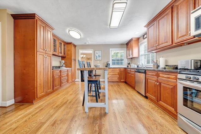 kitchen featuring brown cabinetry, appliances with stainless steel finishes, light wood-type flooring, and baseboards