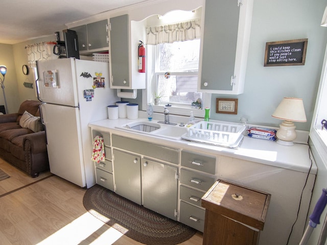 kitchen featuring light wood finished floors, gray cabinets, freestanding refrigerator, a sink, and light countertops