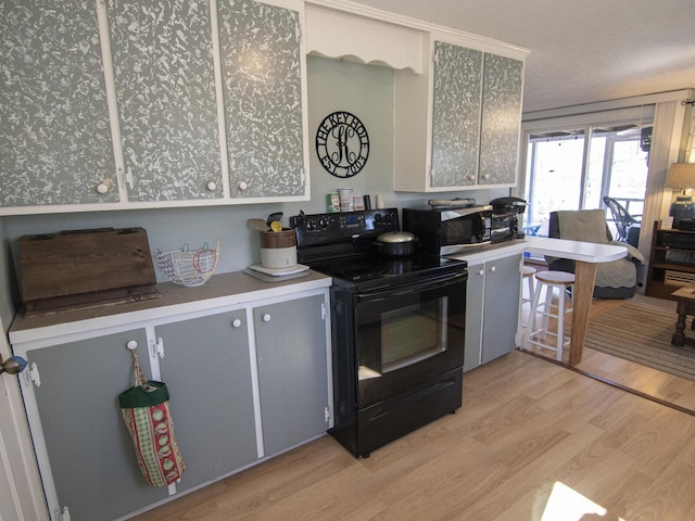 kitchen featuring stainless steel microwave, gray cabinets, light wood-type flooring, and black electric range