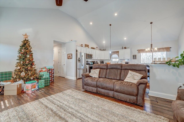 living area with high vaulted ceiling, wood finished floors, and ceiling fan with notable chandelier