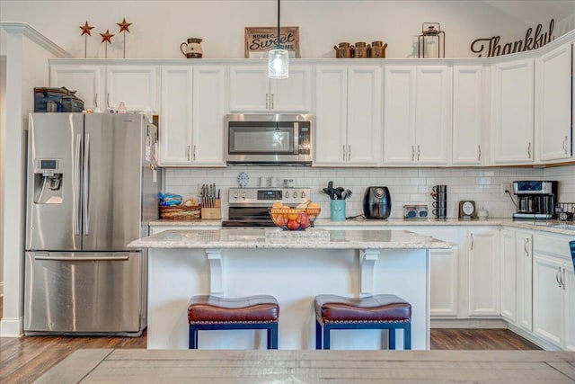 kitchen with backsplash, a kitchen bar, stainless steel appliances, wood finished floors, and white cabinetry