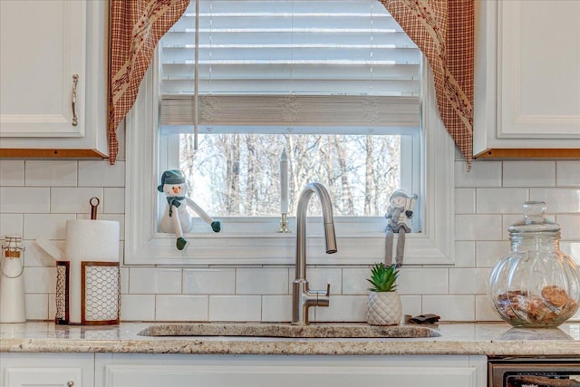 room details featuring tasteful backsplash, white cabinetry, light stone counters, and a sink