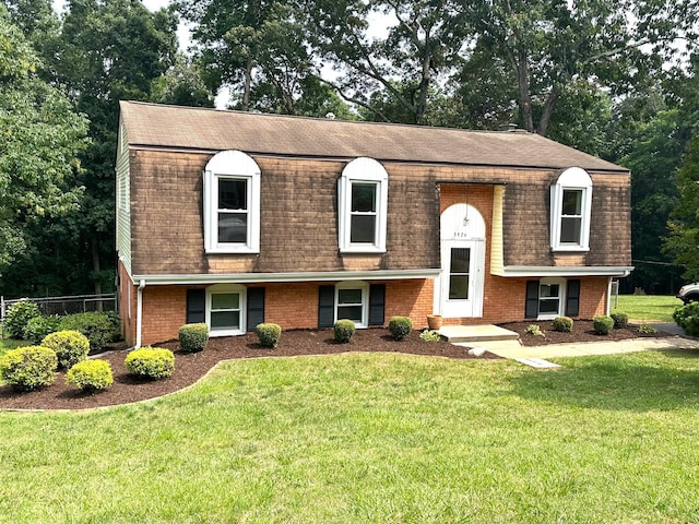 view of front of house featuring a front lawn, fence, brick siding, and roof with shingles