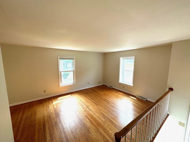 empty room featuring visible vents, a healthy amount of sunlight, baseboards, and wood finished floors