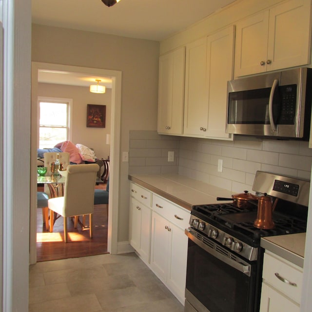 kitchen with stainless steel appliances, backsplash, light countertops, and white cabinetry