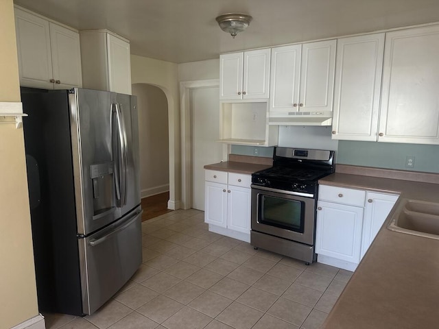 kitchen featuring under cabinet range hood, stainless steel appliances, arched walkways, white cabinetry, and a sink