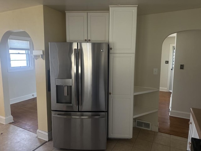 kitchen featuring visible vents, stainless steel fridge, arched walkways, white cabinets, and baseboards