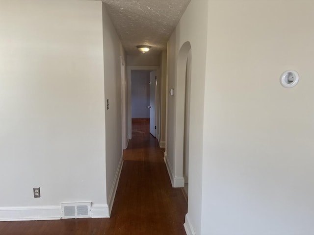 hallway featuring visible vents, baseboards, wood finished floors, arched walkways, and a textured ceiling