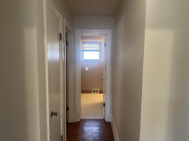 hallway featuring visible vents, baseboards, and dark wood finished floors