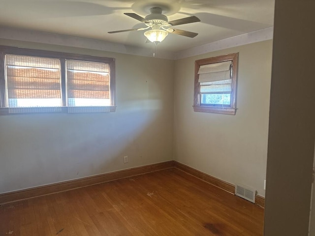 empty room featuring visible vents, baseboards, hardwood / wood-style floors, and a ceiling fan