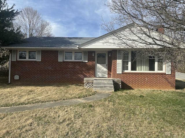 view of front of property with brick siding, a chimney, a front yard, and a shingled roof