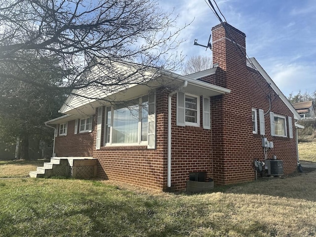 view of side of property with a chimney, brick siding, central AC, and a lawn