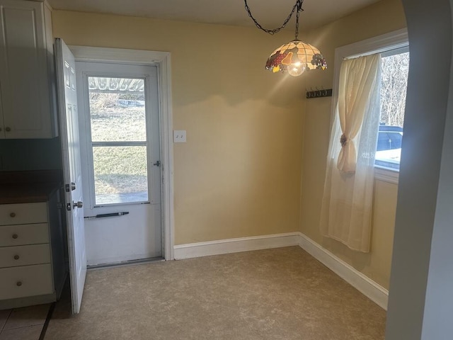 unfurnished dining area featuring baseboards and light colored carpet