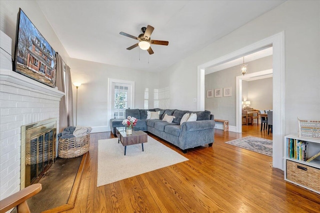 living room with baseboards, wood finished floors, a brick fireplace, and ceiling fan