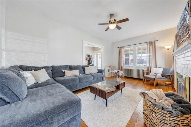 living area featuring a fireplace, radiator heating unit, a ceiling fan, and wood finished floors