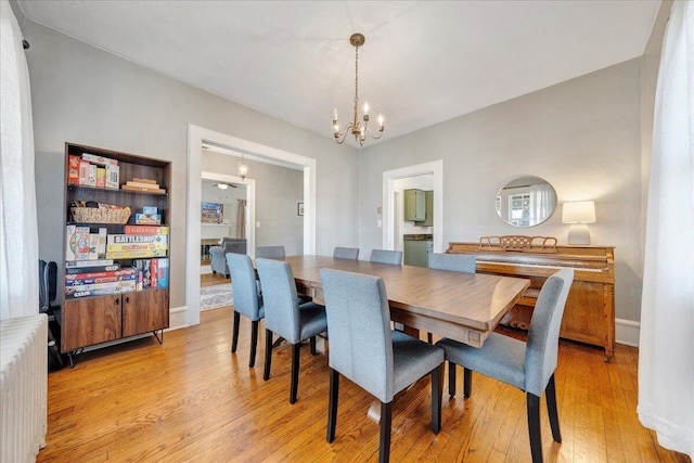 dining area with a chandelier, radiator heating unit, and light wood finished floors