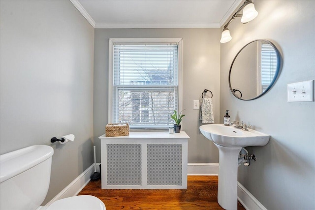 half bath with toilet, radiator, wood finished floors, and ornamental molding