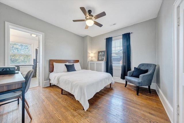 bedroom with a ceiling fan, light wood-style floors, visible vents, and baseboards