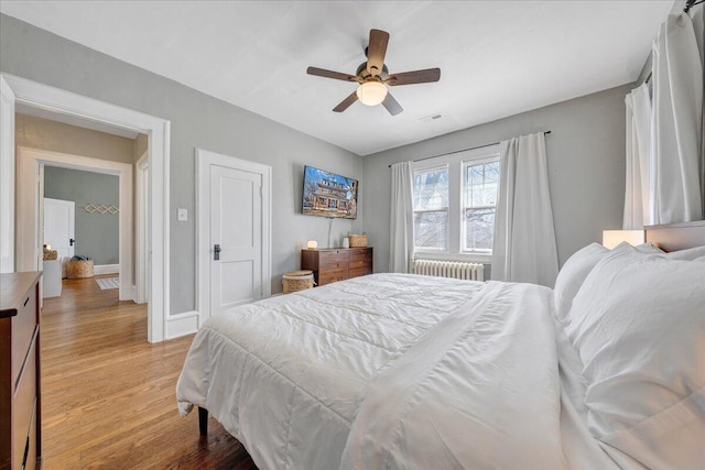 bedroom with light wood-type flooring, visible vents, radiator heating unit, baseboards, and ceiling fan