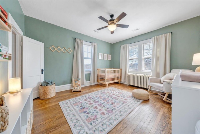 bedroom with a nursery area, radiator heating unit, visible vents, and light wood-type flooring